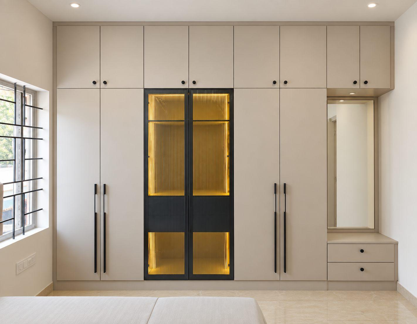 Master bedroom wardrobe in beige laminate with a lit black glass centre unit, long bar handles and a dresser