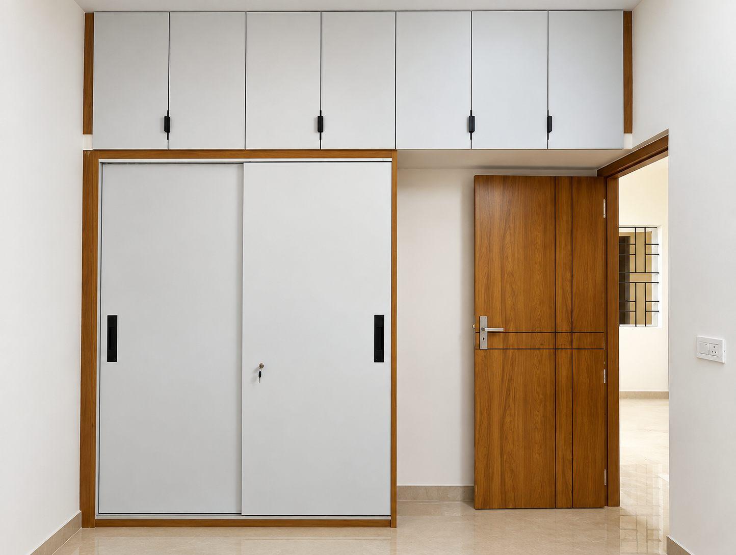 White sliding-door wardrobe with wooden frame and lofts above, beside a wooden bedroom door
